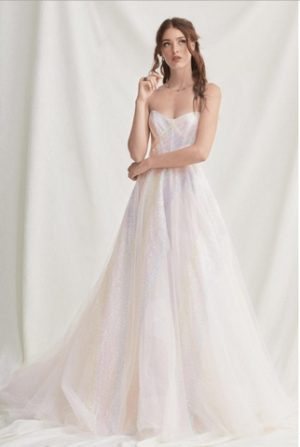 Brünettes Model in einem Corsagentüllkleid mit farbigen Pailleten und Schleppe in einer weißen Fotokulisse von vorne