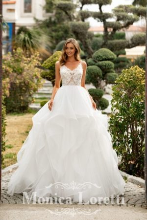 Brünettes Model mit einem weißen Vorantbrautkleid mit Tüllrock und Spitzenoberteil in einem Garten von vorne