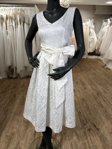 Weißes kurzen Seidenbrautkleid mit V-Ausscnitt und großer Schleife am Gürtel an einer schwarzen Schaufensterpuppe in einem Brautmodenladen