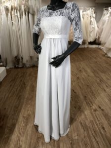 Weißes Schwangerschaftsbrautkleid aus Chiffon mit Spitzenoberteil und halblangen Ärmeln an einer schwarzen Schaufensterpuppe im Brautladen
