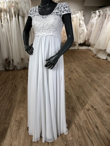 Weißes Schwangerschaftsbrautkleid mit Chiffonrock und Spitzenoberteil und überschnittenen Ärmeln an einer schwarzen Schaufensterpuppe im Brautladen