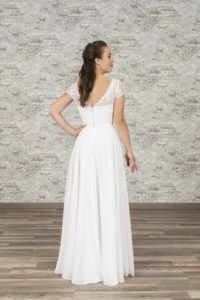 Model mit langen brauenen Haaren in weißem Chiffonbrautkleid mit Bohospitze im Oberteil und kurzen Ärmeln vor bräunlicher Fotokulisse von hinten