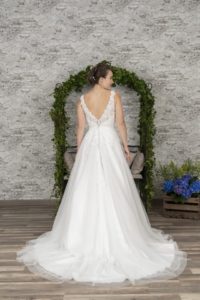 Brünettes Model mit weißem Tüllbrautkleid mit V-Ausschnitt und Trägern in Kulissem mit Traubogen indoor von hinten