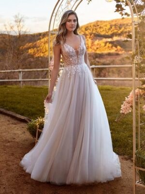 Brünettes Model mit nudefarbenem Tüllbrautkleid mit Spitzenoberteil und V-Ausschnitt vor Gartenkulisse von vorne