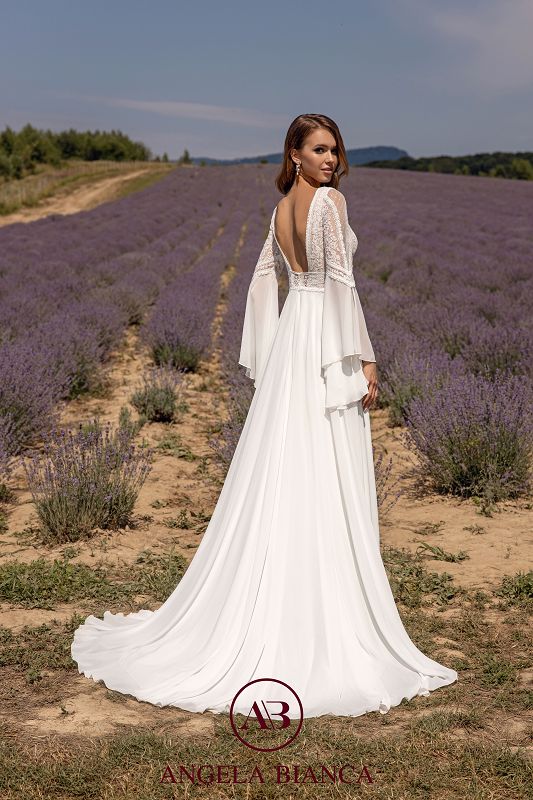 Brünettes Model in einem weißen Boho-Chiffonkleid mit Spitze und tiefem Rückenausschnitt, weiten langen Trompetenärmeln, im Lavendelfeld stehend, von hinten