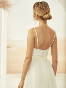 Blondes Model in Spitzencorsage in creme mit Spaghettiträgern und Knopfleiste im Rücken vor hellem Fotohintergrund von hinten