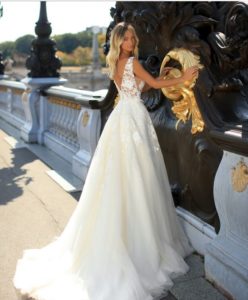 Blondes Model in einem weißen Prinzessinnenkleid mit Spitzenoberteil mit Cutouts und V-Ausschnitt vor einer schloßähnlichen Kulisse von hinten
