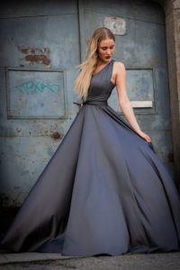 Blondel langhaariges Model in einem grauen, langen Wickelkleid vor einer alten Stahltür