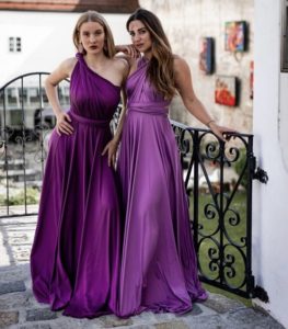 Zwei brünette Frauen mit lilafarbenen, langen Wicklkleidern vor einer Outdoorkulisse mit Geländer
