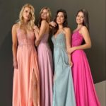 4 langhaarige Models mit Chiffonabendkleidern mit besticken Oberteilen und Spaghettiträgern in apricot, flieder, hellblau und pink vor einem grauen Fotohintergrund