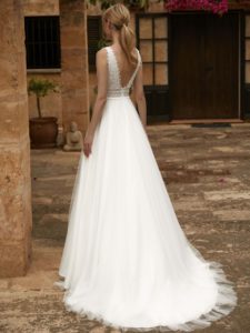 Model mit Zopf in einem weißen Boho-Brautkleid mit Tüllrock und Trägern, betonter Taille und tiefem V-Ausschnitt im Rücken in einem Innenhof von hinten