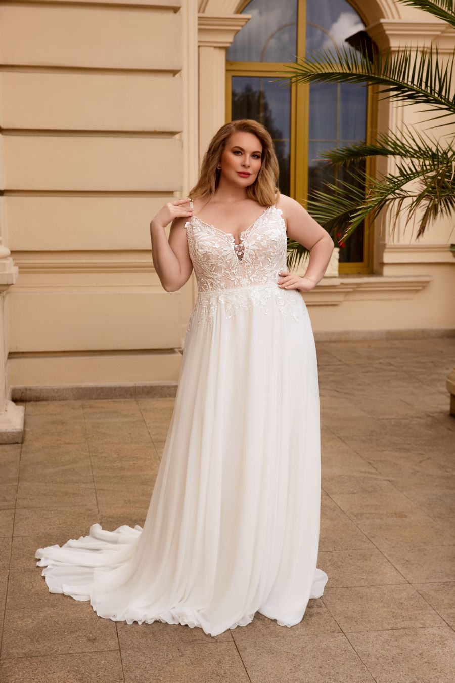 Eine dunkelblonde curvy bride in einem fließenden A-Linien Brautkleid vor einer historischen Mauer